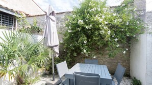 Een terras met een tafel en stoelen, omgeven door planten en een witte muur.
