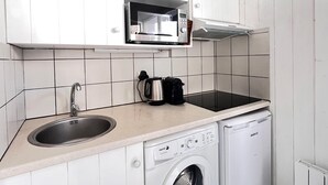 Een kleine keuken met witte kasten, een roestvrijstalen spoelbak, een magnetron, een waterkoker en een vaatwasser.