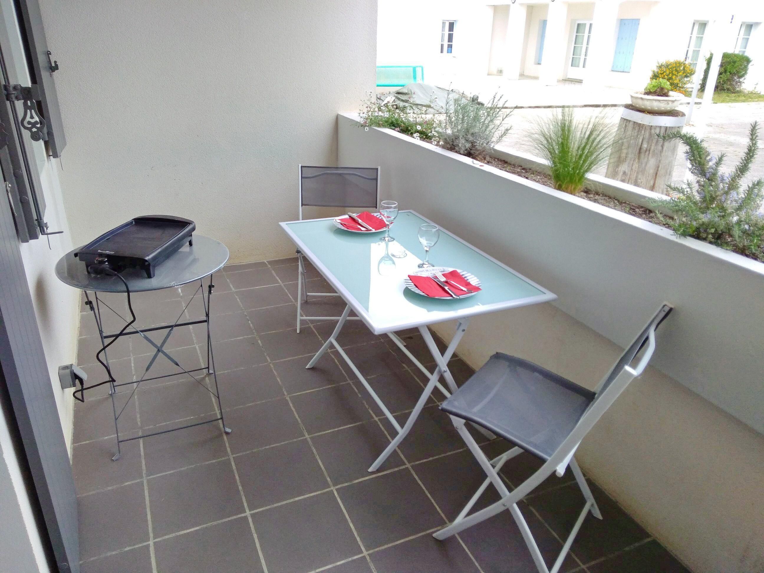 Ein kleiner Balkon mit einem Tisch für zwei Personen, einem Stuhl und einem kleinen Tisch mit einem Lautsprecher.