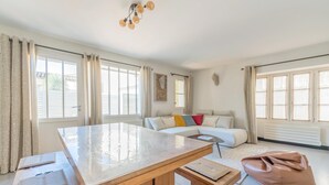 A spacious living room with a large wooden table, a beige sofa with colorful cushions, and a brown bean bag. - House ANNEXE       . (Saint-Martin-de-Ré)
