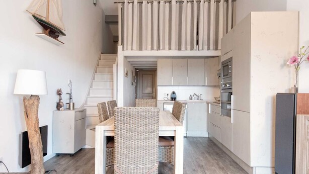 A modern kitchen with a dining area, wooden flooring, and a staircase leading to an upper level. - Appartment PERTUIS . (Saint-Martin-de-Ré)