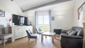 A modern living room with a sofa, two chairs, a coffee table, a TV, and a window with curtains. - Appartment PERTUIS . (Saint-Martin-de-Ré)