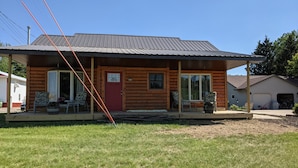 A wooden cabin with a red door, large windows, and a porch with chairs and potted plants.