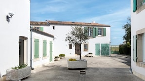 Un patio con un edificio que tiene contraventanas verdes, techo de tejas y un árbol en el centro.