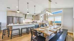 Une cuisine moderne dotée d’un îlot central, d’appareils électroménagers en acier inoxydable et de luminaires suspendus.