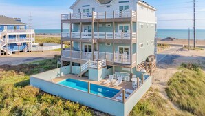 Une propriété en bord de mer, composée de plusieurs étages, dotée d’une piscine, de balcons et d’un accès direct à la plage.