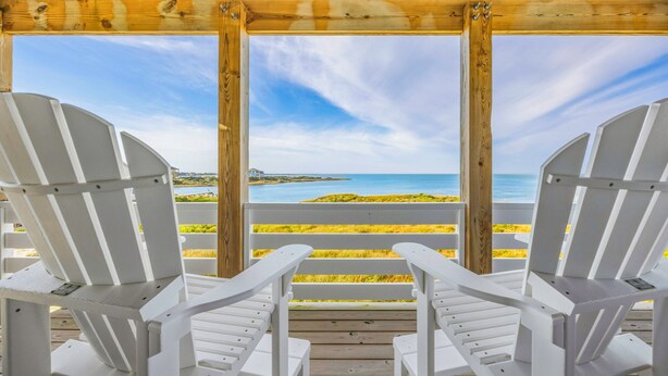 Une terrasse en bois avec deux chaises Adirondack blanches, donnant sur la plage.