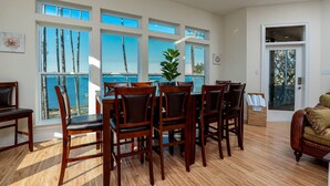 A dining area with a view of the ocean, wooden chairs, a table, and a potted plant. - 🌞😎Pelican Roost - 4 Bedroom Bayfront Home in Fort Morgan!😎🌞 (Gulf Shores)