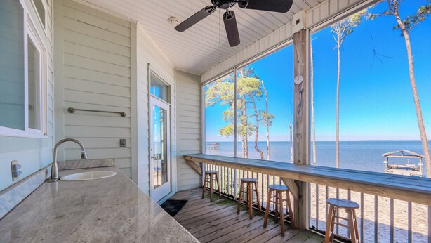 A covered porch with a sink, wooden stools, and a view of the beach. - 🌞😎Pelican Roost - 4 Bedroom Bayfront Home in Fort Morgan!😎🌞 (Gulf Shores)