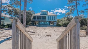 A beach house with a wooden deck and a view of the ocean. - 🌞😎Pelican Roost - 4 Bedroom Bayfront Home in Fort Morgan!😎🌞 (Gulf Shores)