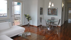 Ein modernes Wohnzimmer mit einem Glastisch, einem weißen Sofa und einem Essbereich mit Tisch und Stühlen.