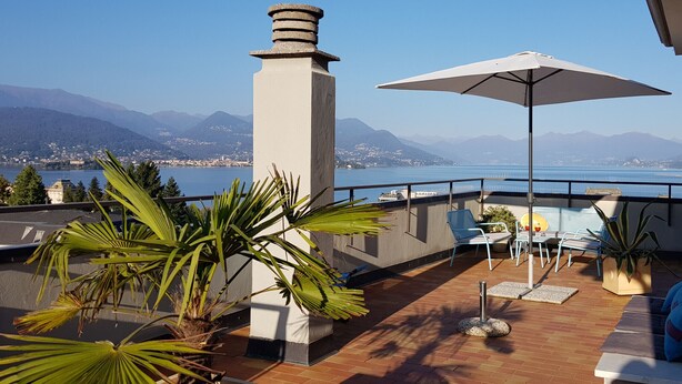 Eine Terrasse mit Blick auf einen See und Berge, ausgestattet mit Gartenmöbeln und Blumentöpfen.