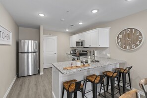 A modern kitchen with a stainless steel refrigerator, white cabinets, a microwave, and a large wall clock. - ALL NEW City Chic Condo (Branson)