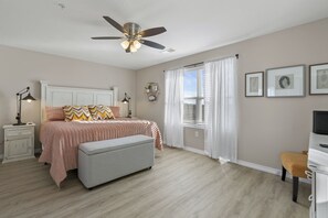 A bedroom with a bed, a bench, a desk, a ceiling fan, and a window with curtains. - ALL NEW City Chic Condo (Branson)