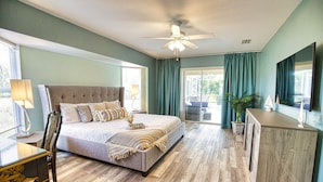 Un dormitorio con cama, escritorio, silla, ventilador de techo y vista al exterior.