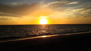 Una puesta de sol sobre un mar tranquilo con una playa en primer plano.