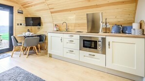 A modern kitchen with wooden ceiling, white cabinets, stainless steel appliances, and a dining area with chairs. - A beautiful and very comfortable glamping experience. (East Haddon)