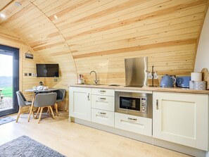 Une cuisine moderne avec un plafond en bois, des armoires blanches, des appareils électroménagers en acier inoxydable et un coin repas avec des chaises.