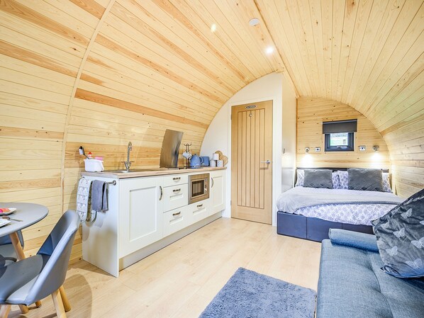 Una cabaña pequeña de madera con kitchenette, comedor y un dormitorio con cama y zona de estar.