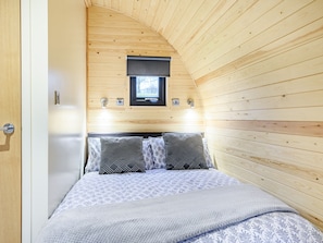 Une chambre avec un plafond en pente en bois, un lit avec une literie à motifs, deux lampes de chevet et une fenêtre au-dessus du lit.