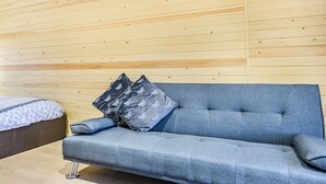 A modern room with a grey sofa, two patterned pillows, and a bed with a patterned blanket. - A beautiful and very comfortable glamping experience. (East Haddon)