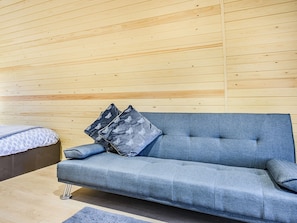 Une chambre moderne avec un canapé gris, deux coussins à motifs et un lit recouvert d’une couverture à motifs.