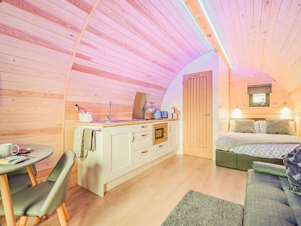 Une petite cabane en bois comprenant un coin cuisine, un lit simple et un petit espace salon.