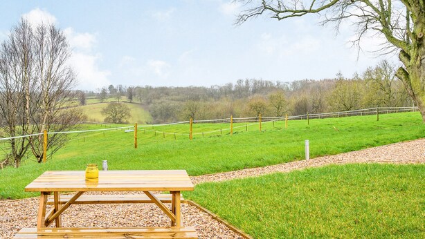 A picnic table with a jar of jam and a bottle of water, surrounded by a grassy field and a fence. - A beautiful and very comfortable glamping experience. (East Haddon)