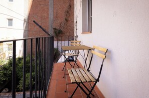 Enjoy a peaceful outdoor space with a balcony featuring a table, two benches, and a window offering a view of the surrounding area.