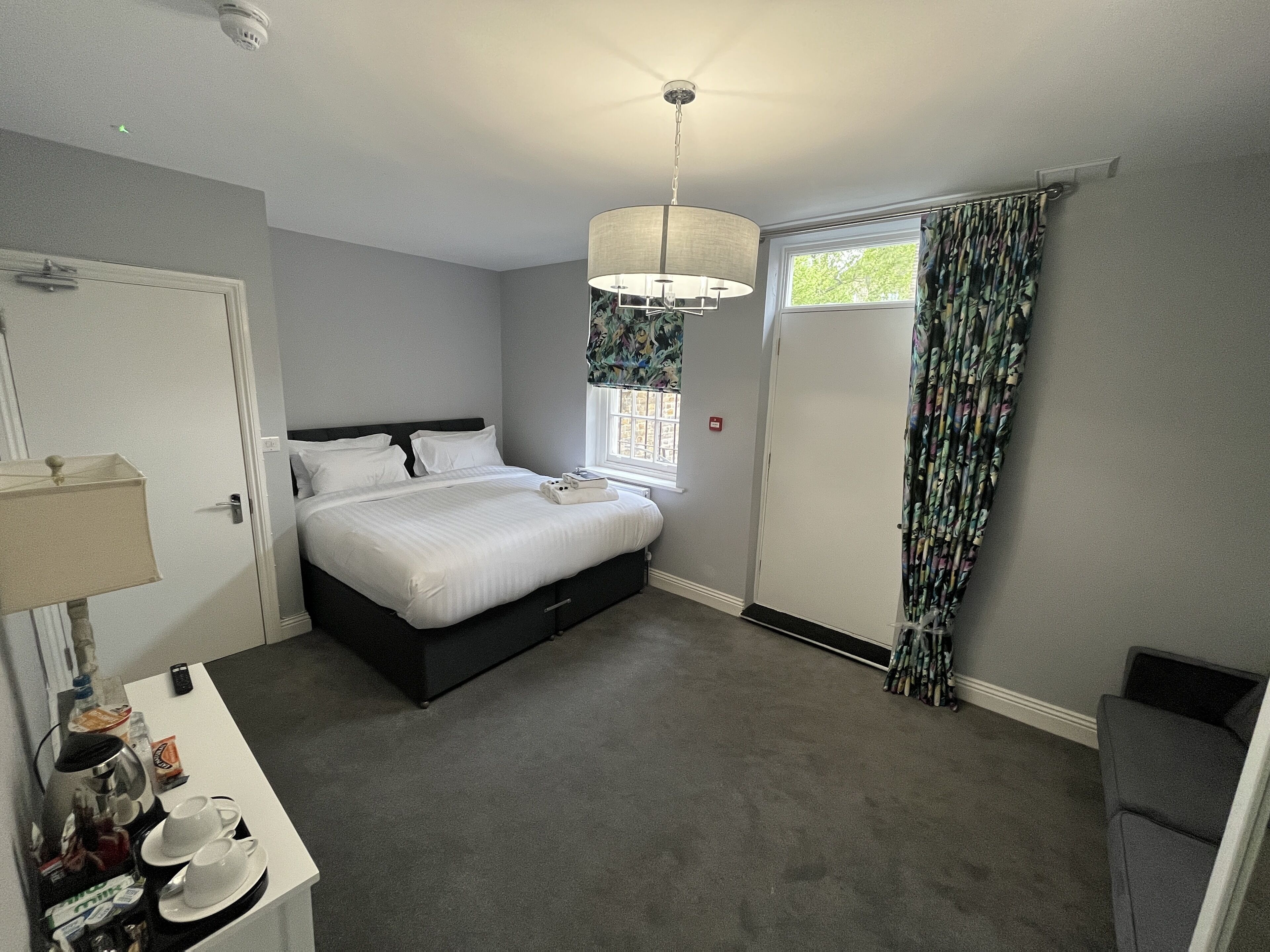 Une chambre à coucher avec un lit, une table de chevet, une lampe et une fenêtre avec des rideaux.