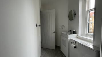 A small, clean bathroom with a white door, a mirror, a sink, and a window.
