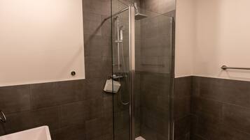 A modern bathroom with a glass-enclosed shower, dark tiles, and a white bathtub.