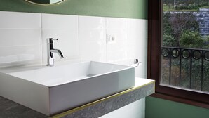 Een badkamer met een witte wastafel, een ronde spiegel en een raam met uitzicht op bomen.