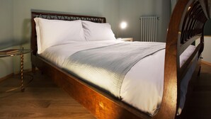 Ein ordentlich bezogenes Bett mit Holzkopfseitenverkleidung, ein Nachttisch mit Lampe und ein Heizkörper im Hintergrund.