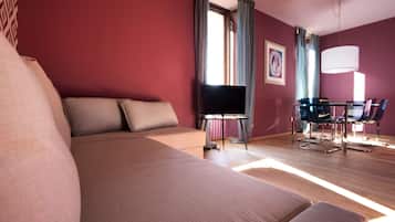 A hotel room with a large bed, a desk with a flat-screen TV, a chair, and a table.