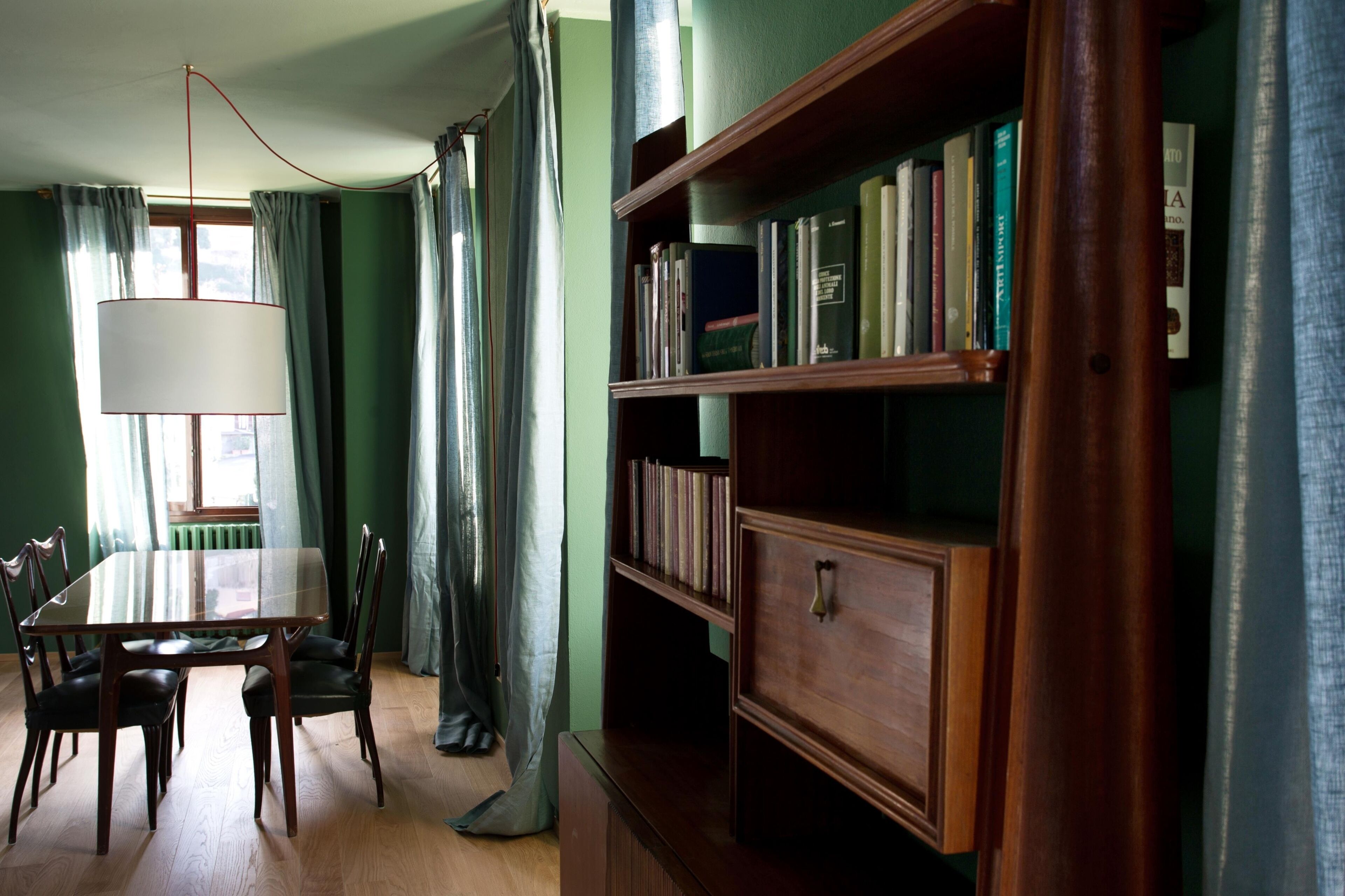 Um quarto com uma mesa e cadeiras de madeira, uma estante e uma janela com cortinas.