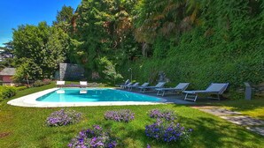A swimming pool with lounge chairs and purple flowers in a landscaped garden. - Suite "Anguilla" at 2 steps from the lake with panoramic view. Lounge bar and swimming pool (Faggeto Lario)