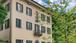 A multi-story building with a beige facade, green shutters, and a central entrance with a decorative arch. - Suite "Anguilla" at 2 steps from the lake with panoramic view. Lounge bar and swimming pool (Faggeto Lario)
