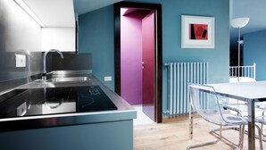 A modern kitchen with a built-in stove, a dining area with a white table and clear chairs, and a door leading to a room with a pink wall. - Suite "Persico" at 2 steps from the lake with private terrace, lounge bar and swimming pool (Faggeto Lario)
