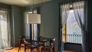 A room with a dining table and chairs, a hanging lamp, and a view of a lake through large windows. - Suite "Luccio" at 2 steps from the lake with panoramic view. Lounge bar and swimming pool (Faggetto  Lario)
