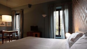 A hotel room with a large bed, a desk with a chair, a television, and a lamp.