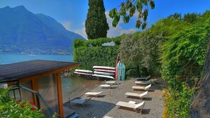 Eine Terrasse mit Liegestühlen, ein kleines Gebäude und der Blick auf einen See und Berge.