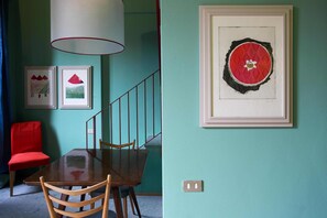 A dining area with a wooden table and chairs, a red chair, and framed artwork on the wall.