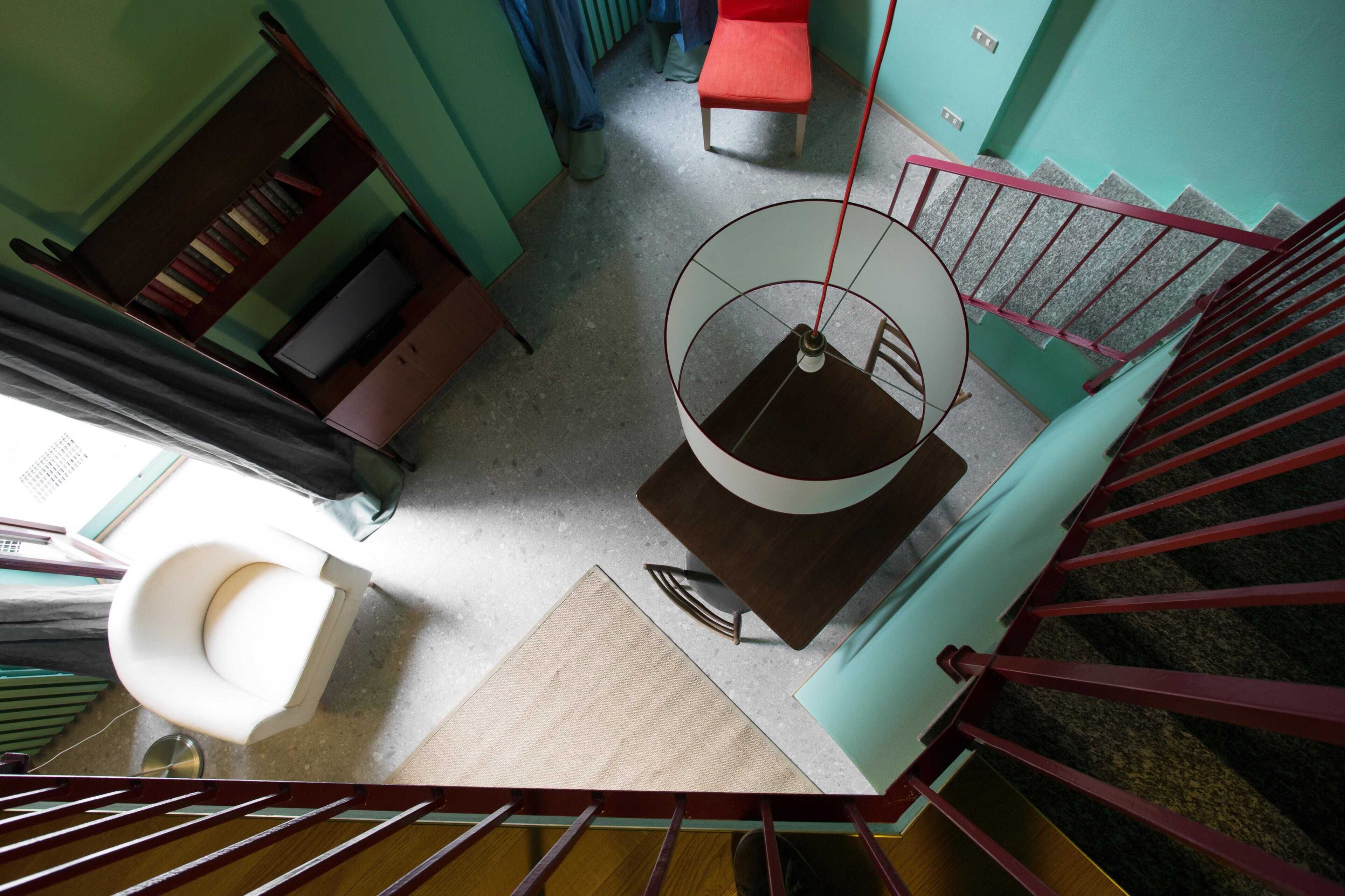 Una habitación con una escalera, un inodoro blanco, un armario de madera y una silla roja.
