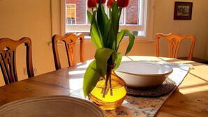 Ein Esstisch mit einer Schüssel, einer Vase mit Blumen und einem Fenster mit Blick auf ein Backsteingebäude.