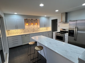 Una cocina moderna con gabinetes grises, encimera de mármol, estufa integrada y refrigerador de acero inoxidable.