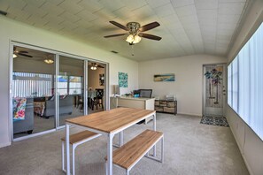 A spacious room with a ceiling fan, a wooden table with benches, a desk with a computer, and a door with a decorative mat. - Pool Access: Ranch-Style House in Sun City Center (Sun City Center)