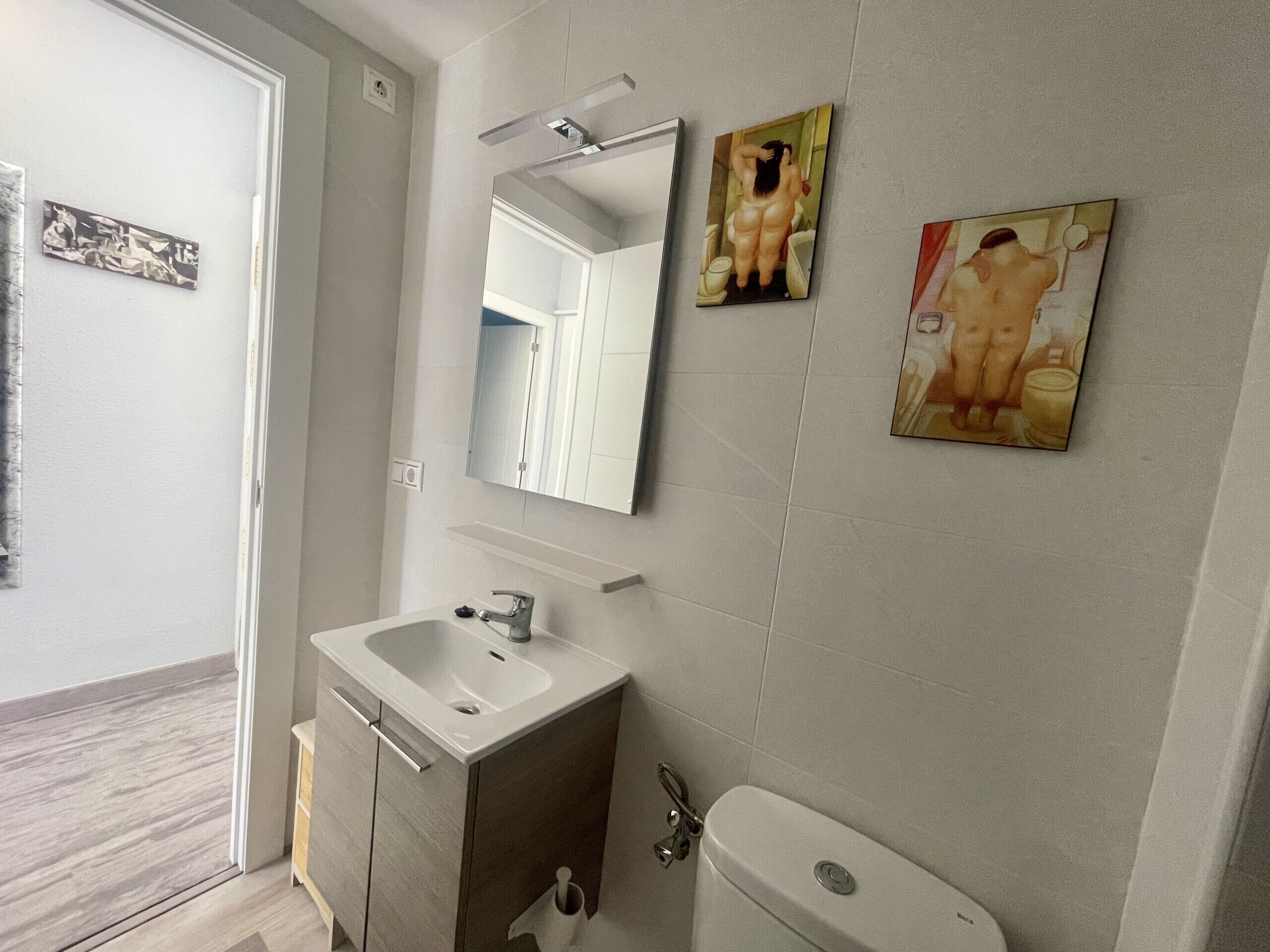 Un baño con lavamanos, espejo, inodoro y dos cuadros colgados en la pared.