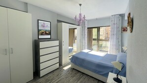 Un dormitorio con cama, cómoda, armario, candelabro y ventana con cortinas.