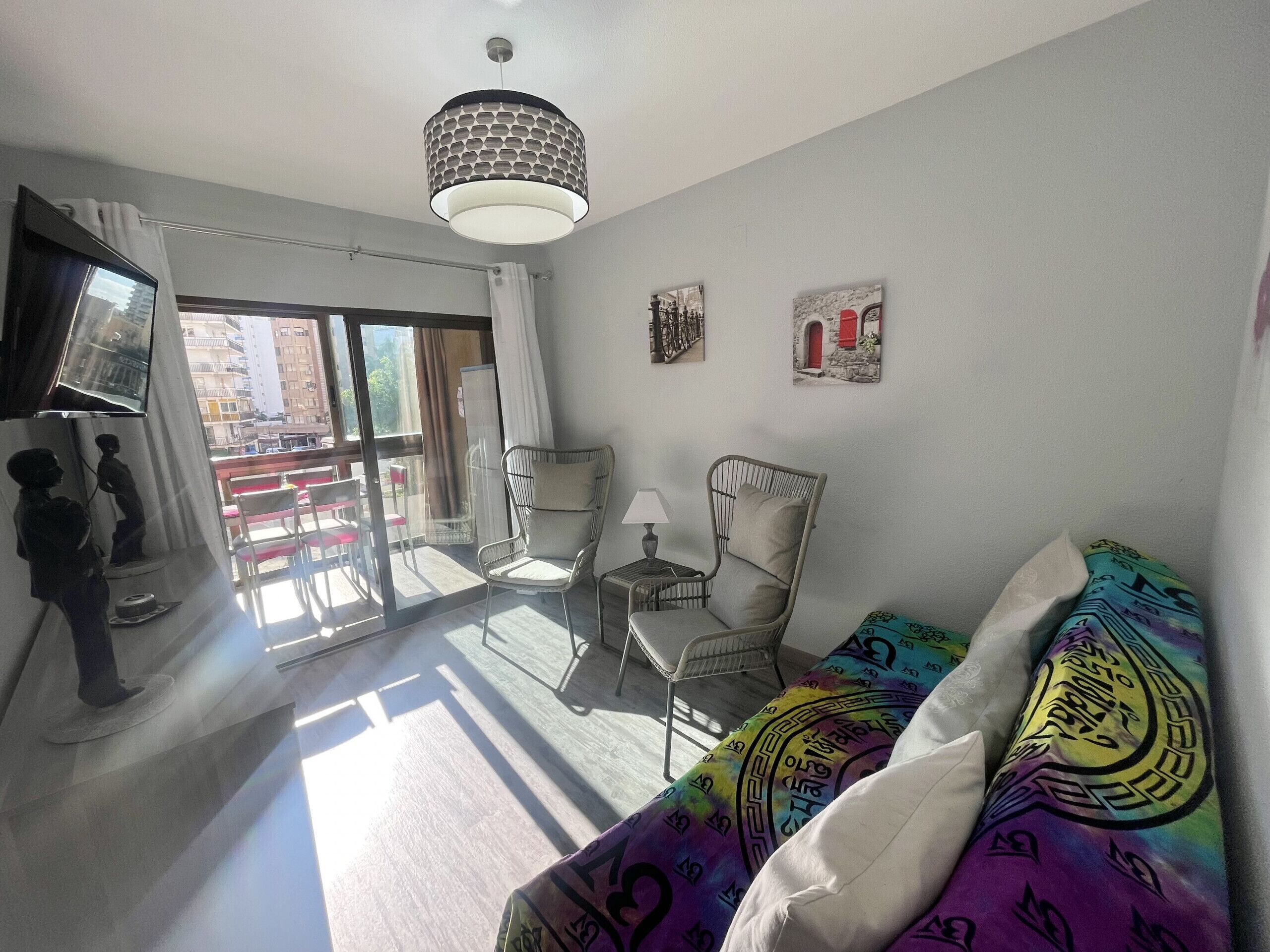 A modern living room with a sofa, a chair, a TV, and a balcony with a view of the city.